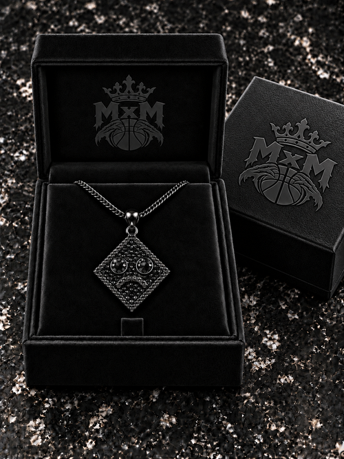 All-black MxM sad-face necklace in black velvet box with embossed crest inside and on outer lid
