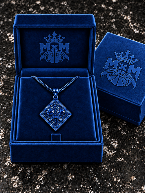 Blue MxM sad-face necklace in matching velvet box with crests inside and outside