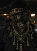 MxM olive and black spiderweb keffiyeh on a model with prominent spider face motif, crowned MxM basketball logo and thin knotted tassels. Digital design preview, not a manufactured sample photo.