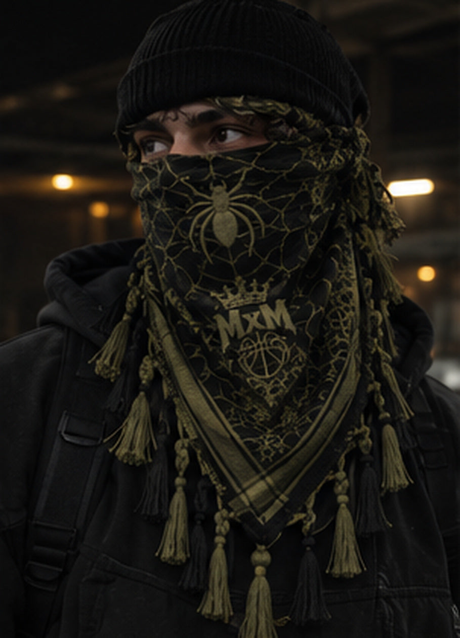 MxM olive and black spiderweb keffiyeh on a model with prominent spider face motif, crowned MxM basketball logo and thin knotted tassels. Digital design preview, not a manufactured sample photo.