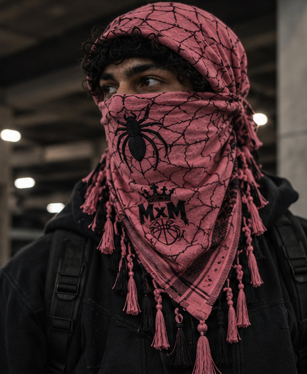 MxM pink and black spiderweb keffiyeh on a model with prominent spider face motif, crowned MxM basketball logo and thin knotted tassels. Digital design preview, not a manufactured sample photo.