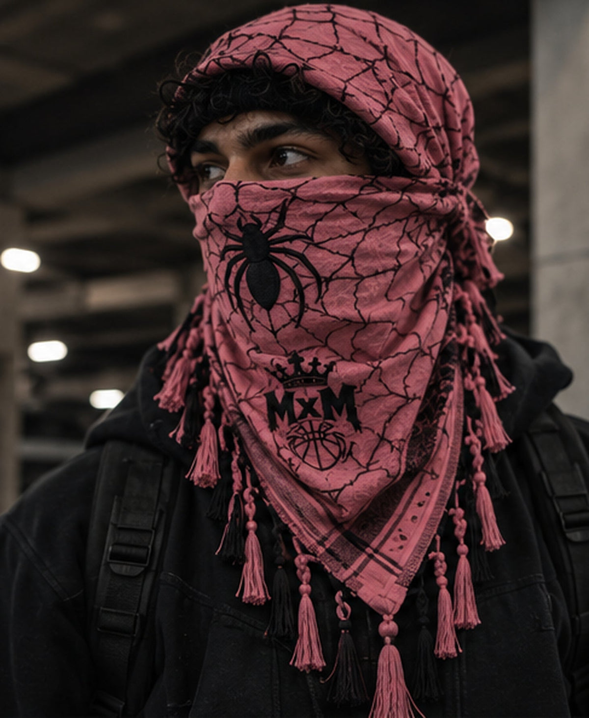 MxM pink and black spiderweb keffiyeh on a model with prominent spider face motif, crowned MxM basketball logo and thin knotted tassels. Digital design preview, not a manufactured sample photo.