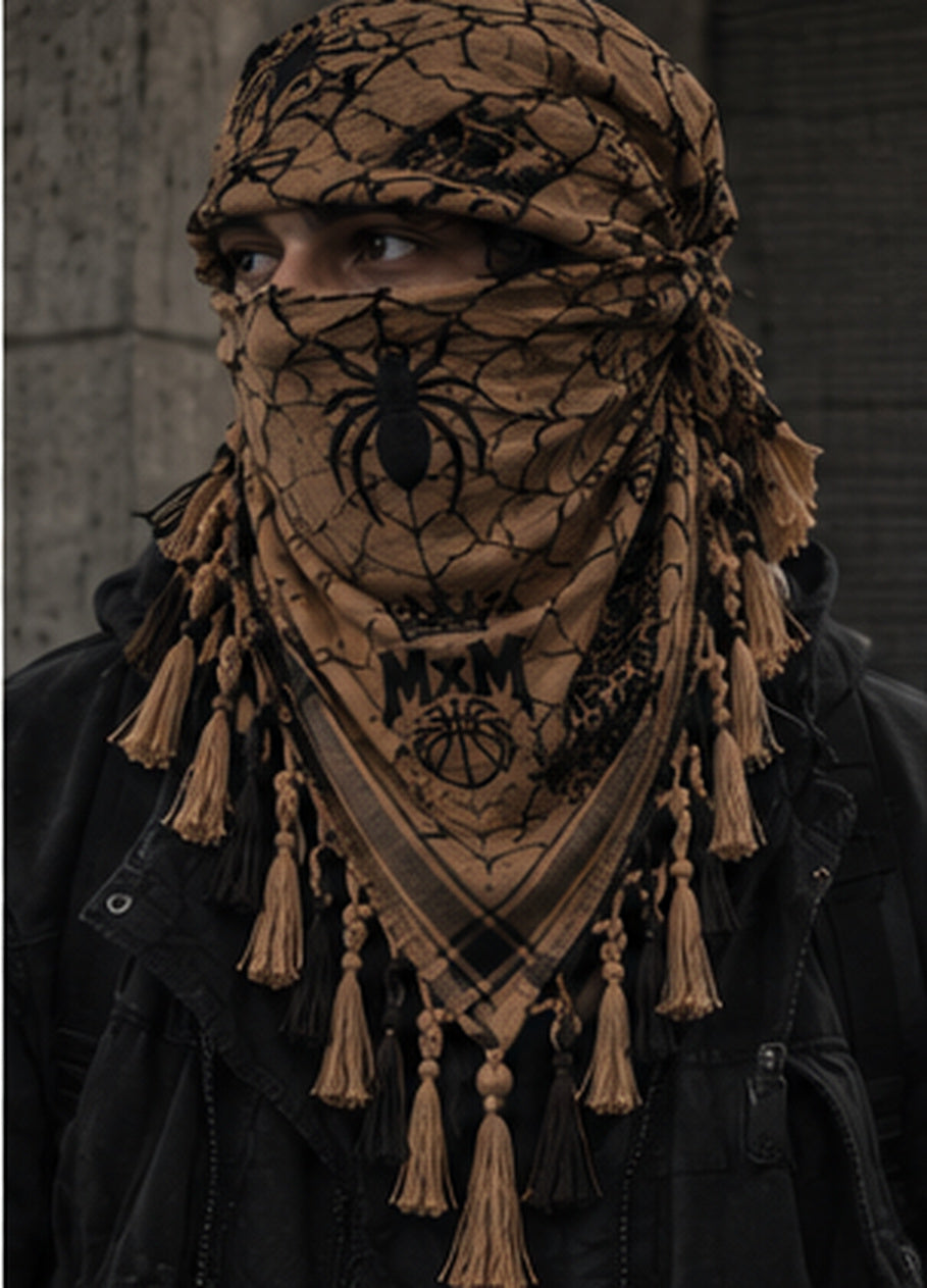 MxM tan and black spiderweb keffiyeh on a model with prominent spider face motif, crowned MxM basketball logo and thin knotted tassels. Digital design preview, not a manufactured sample photo.
