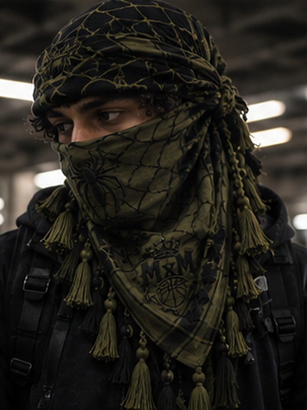 MxM spiderweb keffiyeh olive model styling concept: face spider, crowned MxM basketball logo, triangular web pattern and knotted tassel fringe. Digitally rendered, not a manufactured sample photo.