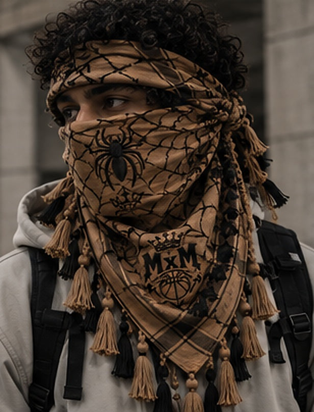MxM spiderweb keffiyeh tan model styling concept: face spider, crowned MxM basketball logo, triangular web pattern and knotted tassel fringe. Digitally rendered, not a manufactured sample photo.