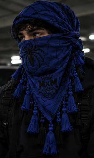 MxM navy blue keffiyeh on a model with spider face, web pattern, crowned MxM emblem and hanging tassels. Digital preorder design mockup, not a physical sample photo.