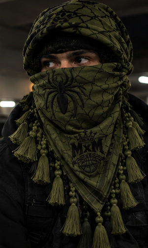 MxM olive black keffiyeh on a model with spider face, web pattern, crowned MxM emblem and hanging tassels. Digital preorder design mockup, not a physical sample photo.