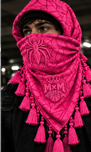 MxM pink keffiyeh on a model with spider face, web pattern, crowned MxM emblem and hanging tassels. Digital preorder design mockup, not a physical sample photo.