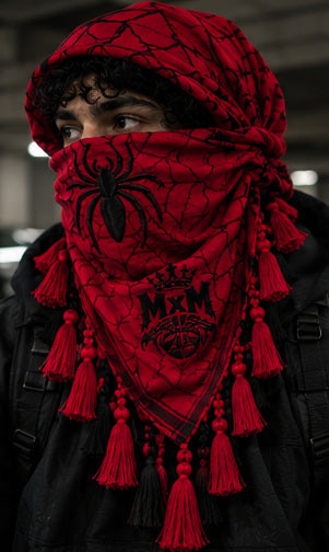 MxM red black keffiyeh on a model with spider face, web pattern, crowned MxM emblem and hanging tassels. Digital preorder design mockup, not a physical sample photo.