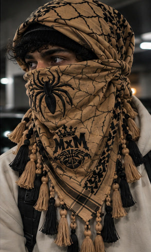 MxM tan black keffiyeh on a model with spider face, web pattern, crowned MxM emblem and hanging tassels. Digital preorder design mockup, not a physical sample photo.