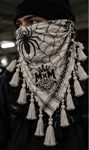 MxM white black keffiyeh on a model with spider face, web pattern, crowned MxM emblem and hanging tassels. Digital preorder design mockup, not a physical sample photo.