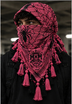 MxM webbed keffiyeh pink black model front. Crowned MxM logo appears on front only; back features woven web pattern and knotted fringe; photorealistic preorder design mockup.