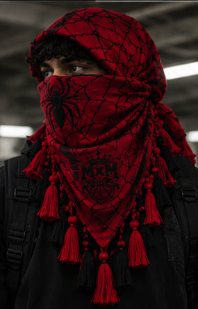 MxM webbed keffiyeh red black model front. Crowned MxM logo appears on front only; back features woven web pattern and knotted fringe; photorealistic preorder design mockup.
