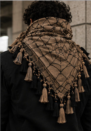 MxM webbed keffiyeh tan black model back. Crowned MxM logo appears on front only; back features woven web pattern and knotted fringe; photorealistic preorder design mockup.