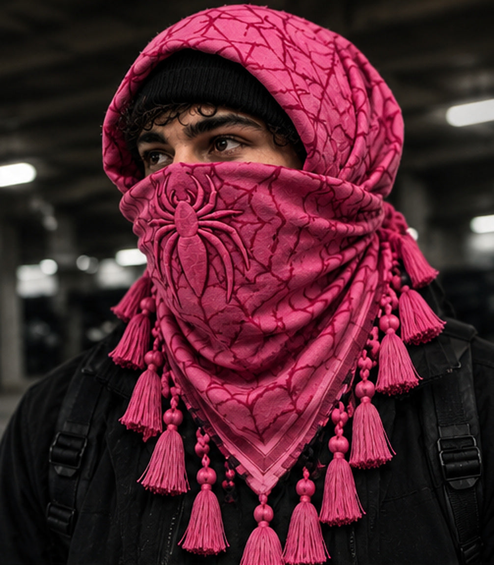 Pink MxM spiderweb keffiyeh on model, front: spider design on the face covering; knotted tassel trim; photorealistic design preview, not a photographed manufactured sample.
