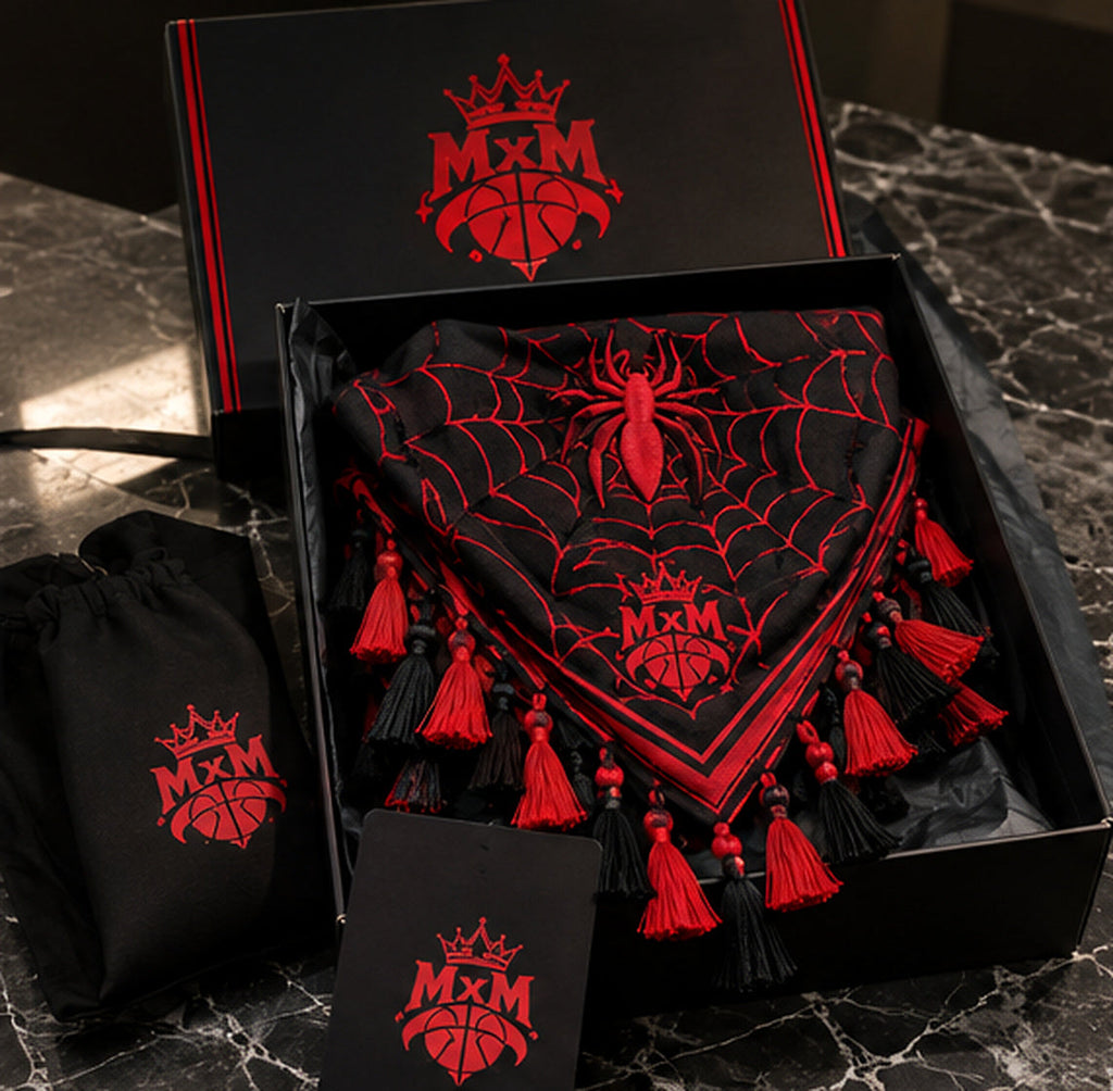 Black and red MxM spider-web keffiyah folded in matching branded packaging with front spider, web pattern and tassels. Packaging concept visualization.